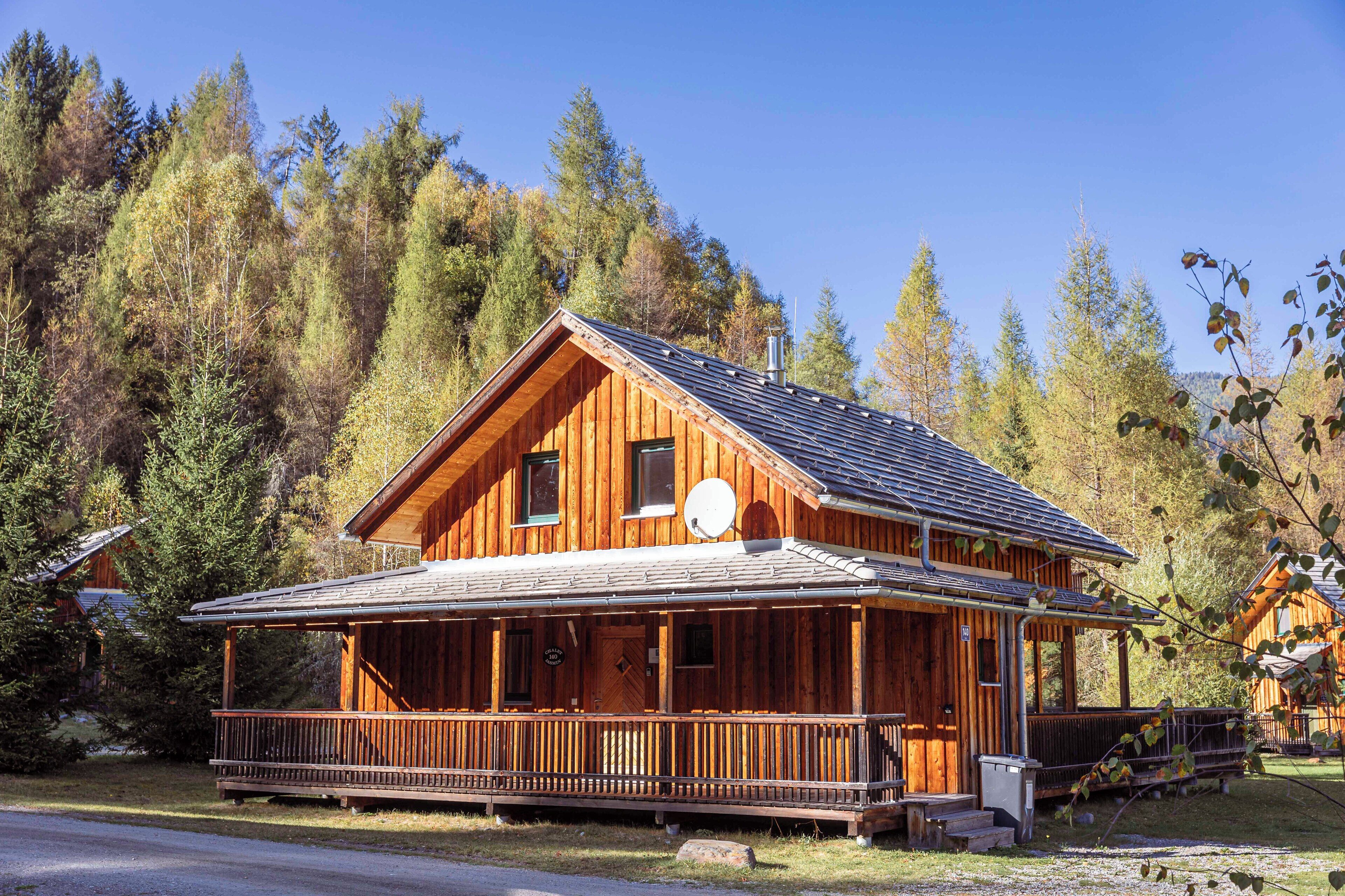 A wooden cabin with a porch, surrounded by trees.