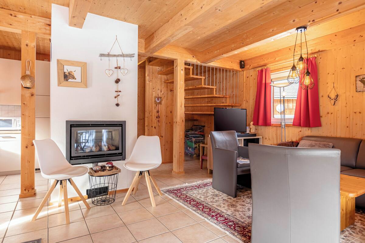 Un interior de madera con chimenea, zona de estar y una escalera.