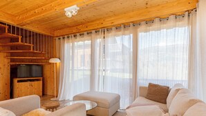 L'intérieur d'un chalet en bois chaleureux et accueillant, avec un canapé, un pouf et un téléviseur posé sur un meuble en bois.