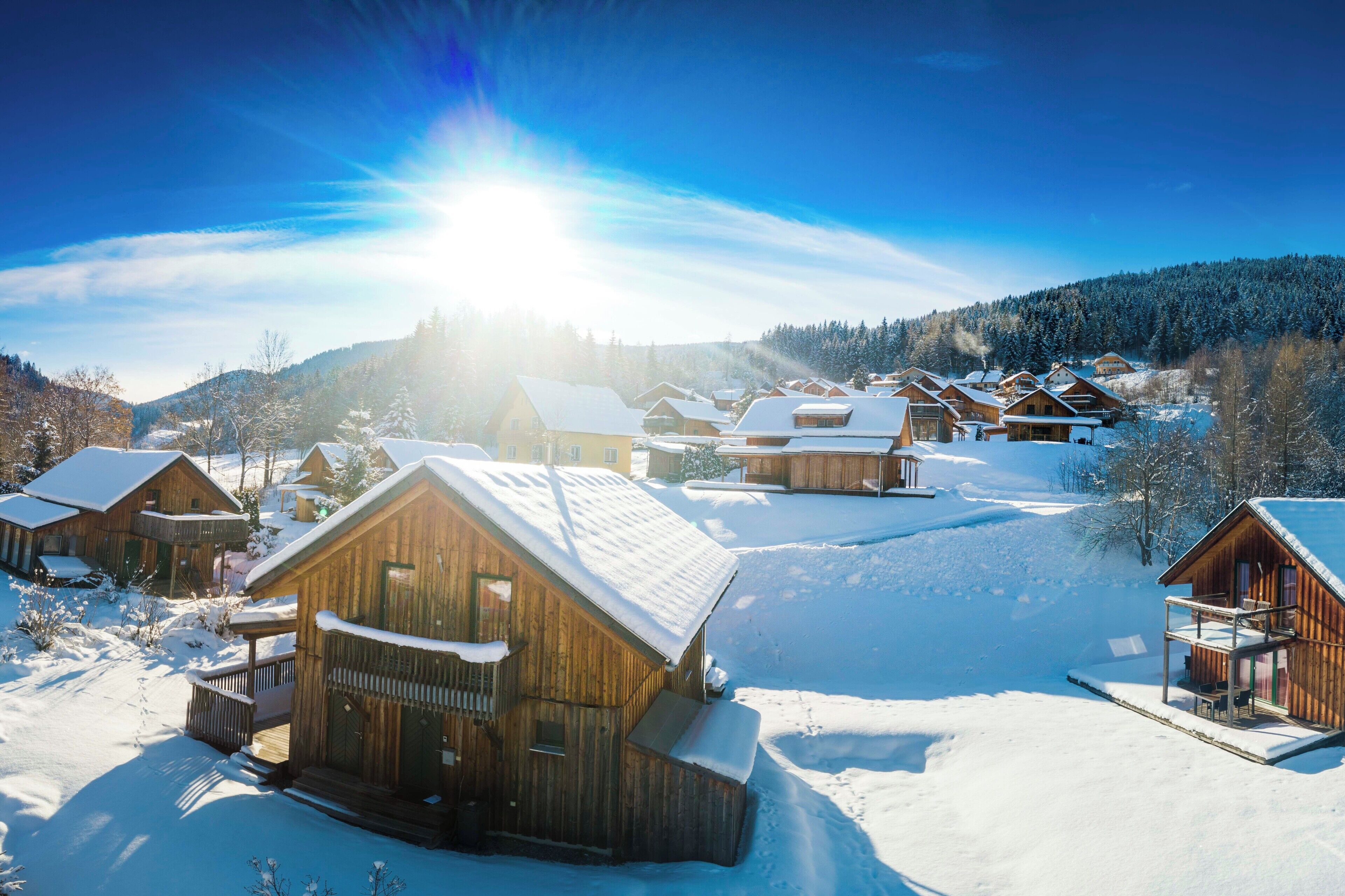 Un villaggio innevato con case di legno, cielo sereno e montagne sullo sfondo.