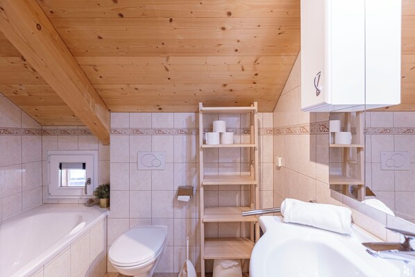 A bathroom with a wooden ceiling, a toilet, a sink, and a shelf with toiletries. - Almdorf Stadl by ALPS RESORTS (Stadl an der Mur)