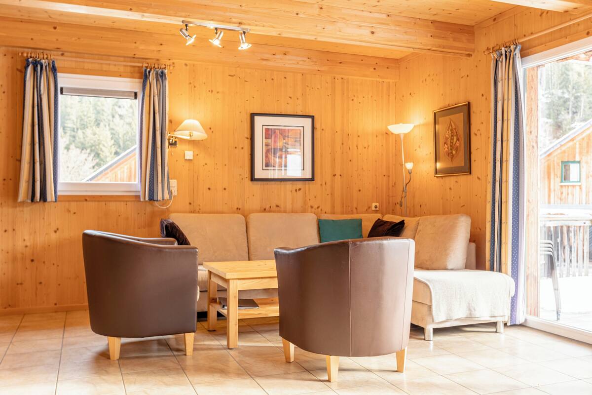 Un interior de madera con un sofá, dos sillones, una mesa y una lámpara.