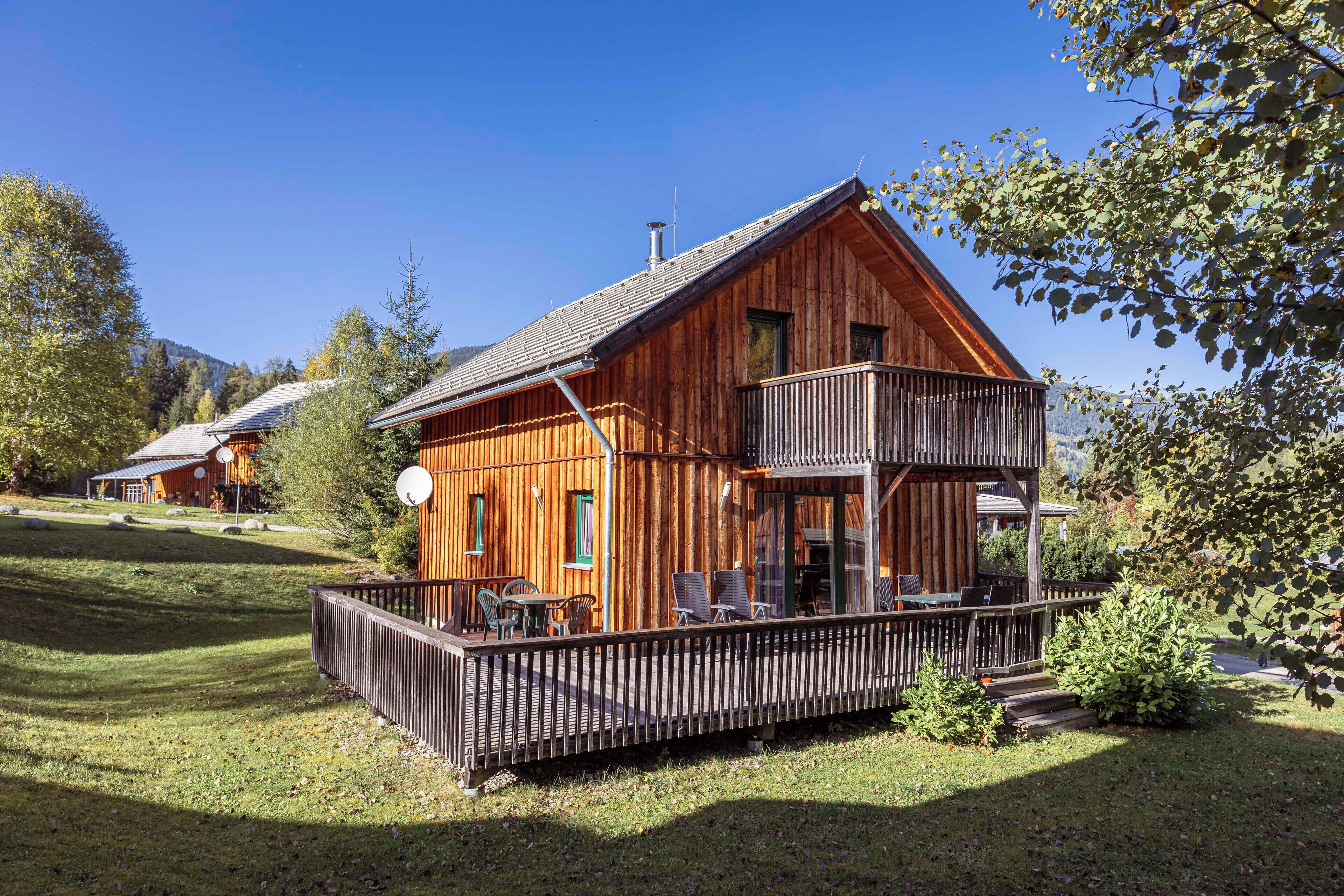 Une cabane en bois dotée d’un balcon, entourée d’une terrasse délimitée par une clôture et d’une cour gazonnée.