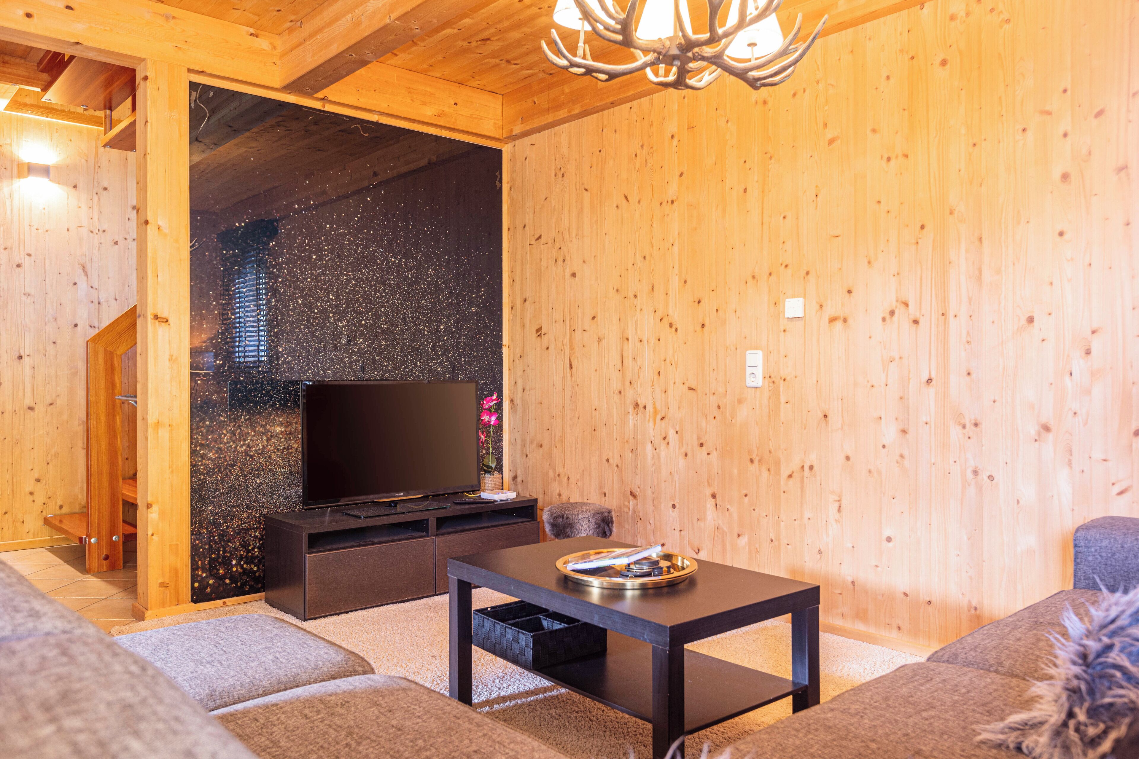 A cozy living room with a wooden interior, a flat-screen TV on a black stand, a small table with a tray, and a sofa.