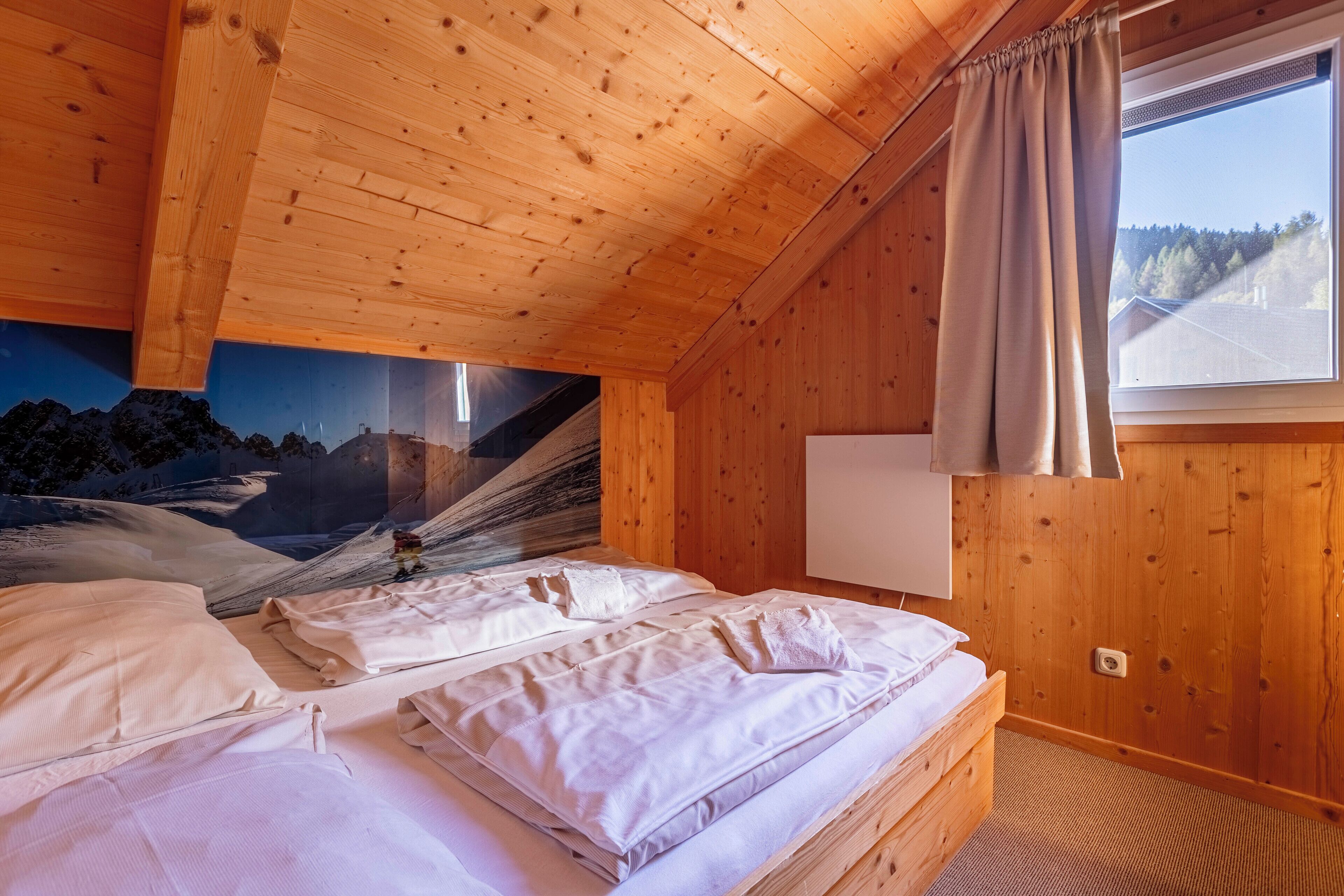 A wooden cabin bedroom with a bed, a window with curtains, and a mural on the wall.