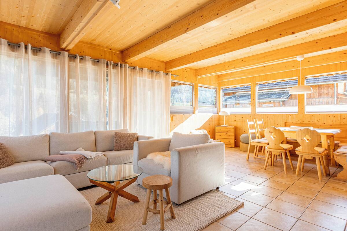Acogedor interior de cabaña de madera con sala de estar, comedor y ventanas amplias.