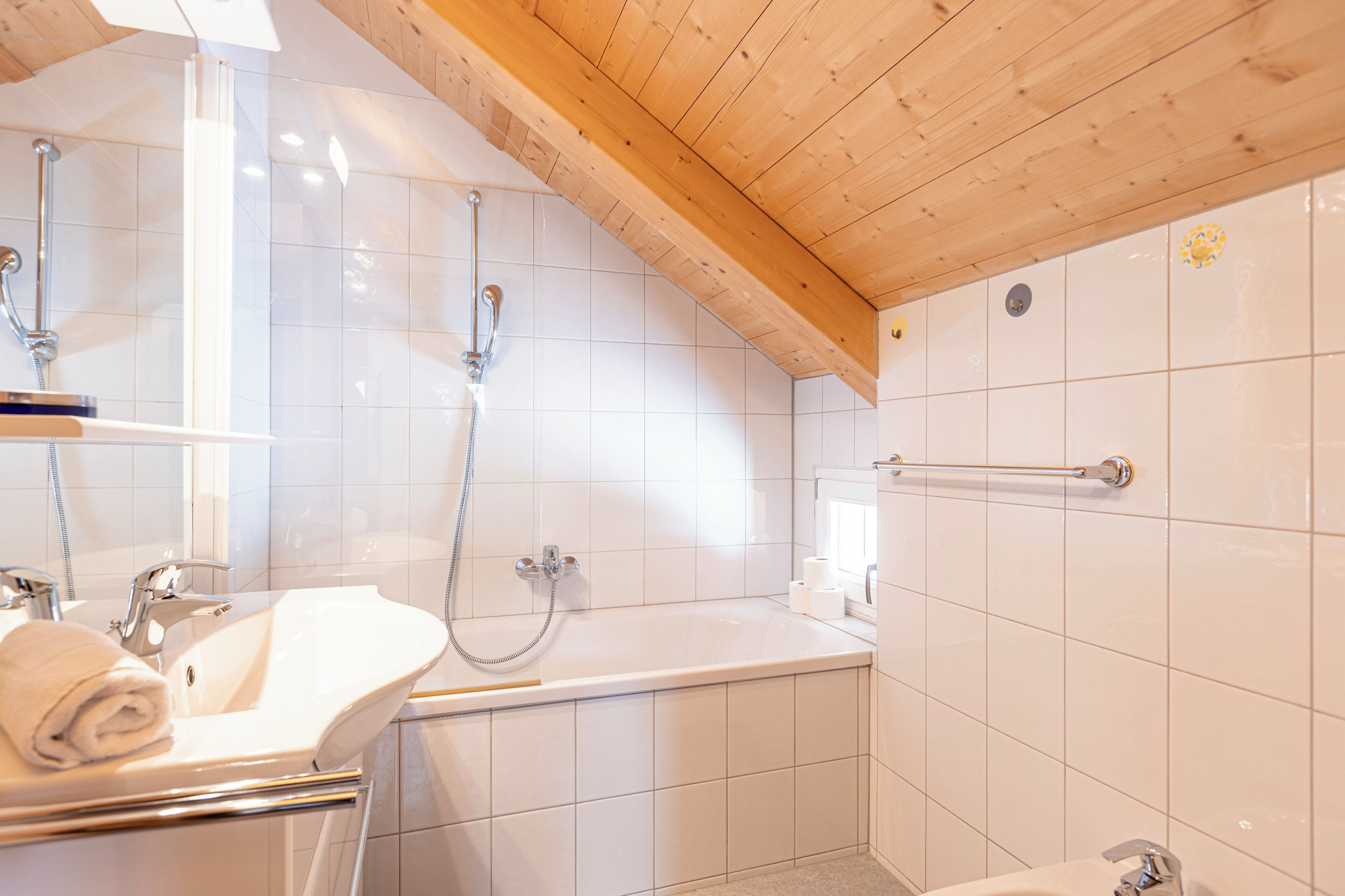 A bathroom with a wooden ceiling, white tiles, a bathtub, a sink, and a shower.