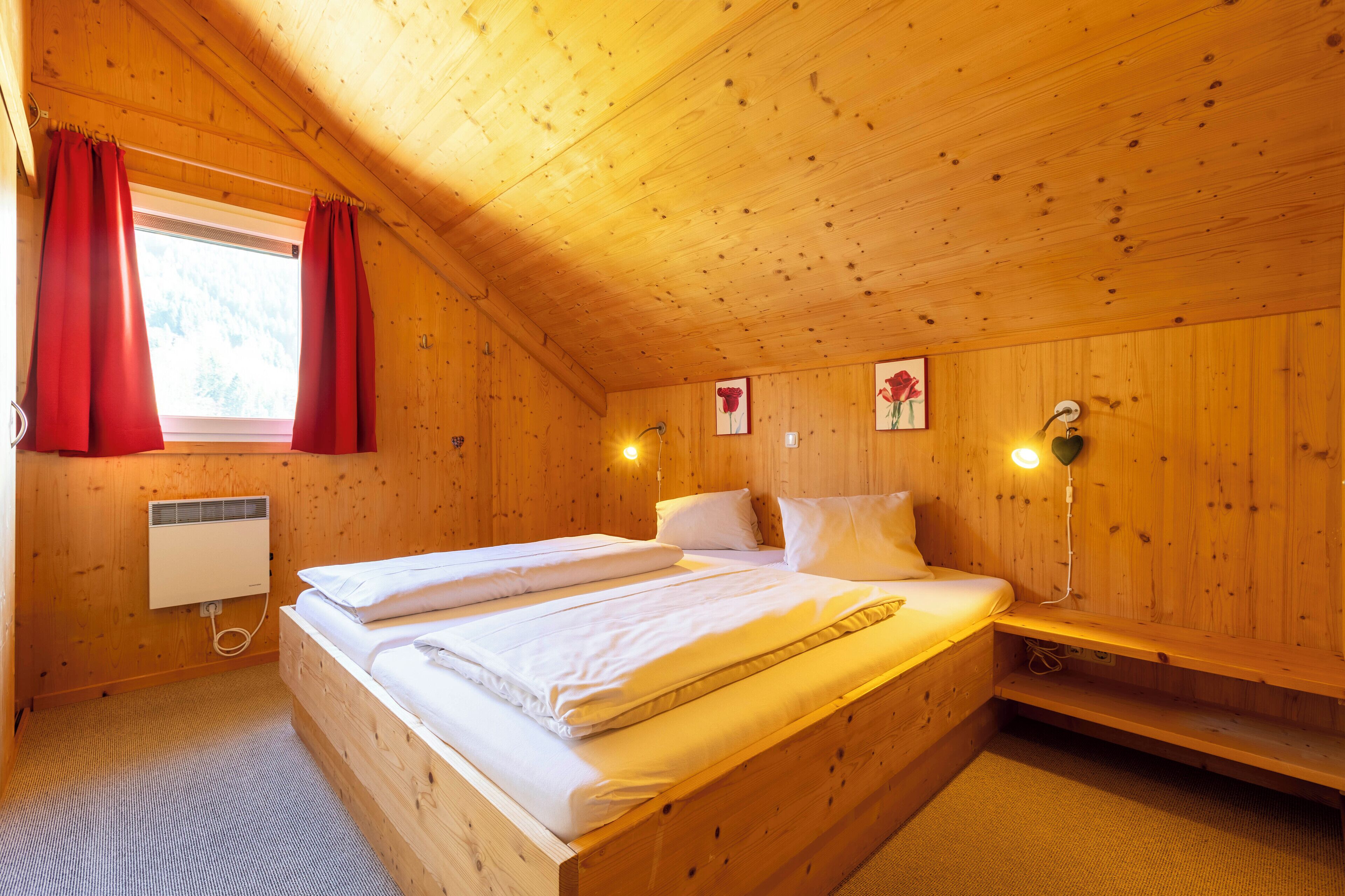 Ein Zimmer in einer Holzhütte mit einem Bett, roten Vorhängen, einer Wandheizung und einem Bild mit Blumen.