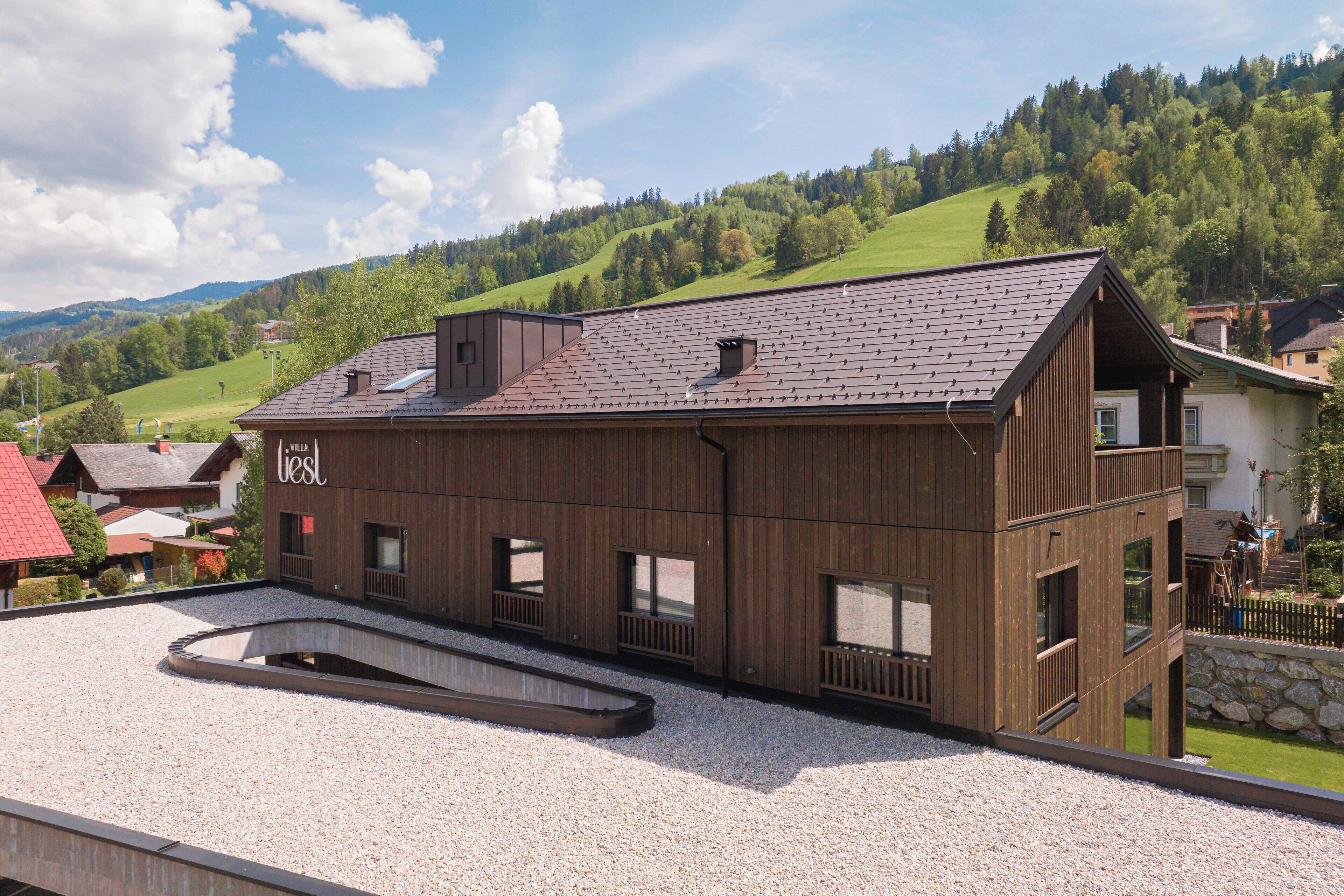 Ein modernes Gebäude mit geneigtem Dach, Holzfassade und zahlreichen Fenstern.