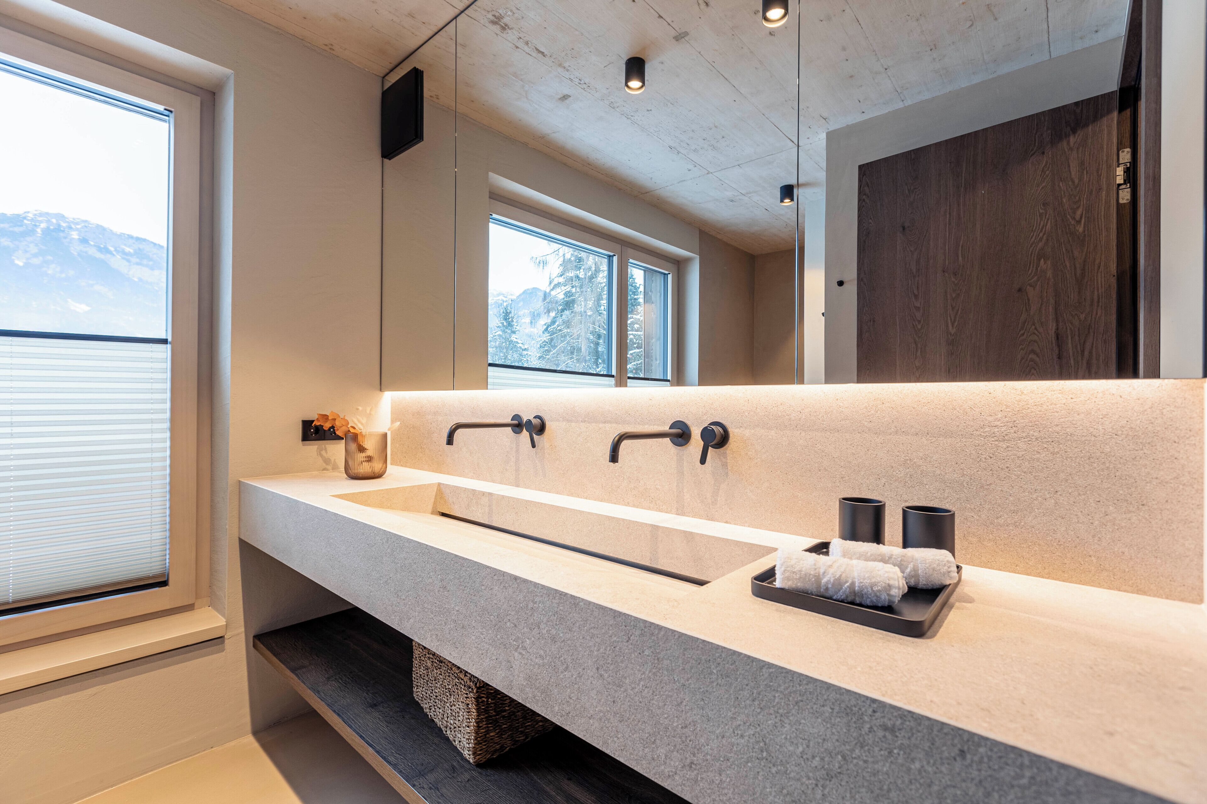 Ein modernes Badezimmer mit einem großen Spiegel, einem Doppelwaschbecken und einem Fenster mit Bergblick.