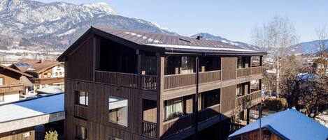 A multi-story wooden building with balconies, set against a mountainous backdrop.