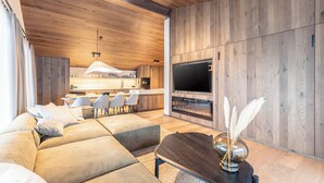 Een moderne woonkamer met een ruime hoekbank, een bijzettafeltje en een flatscreen televisie bevestigd aan een houten wand.