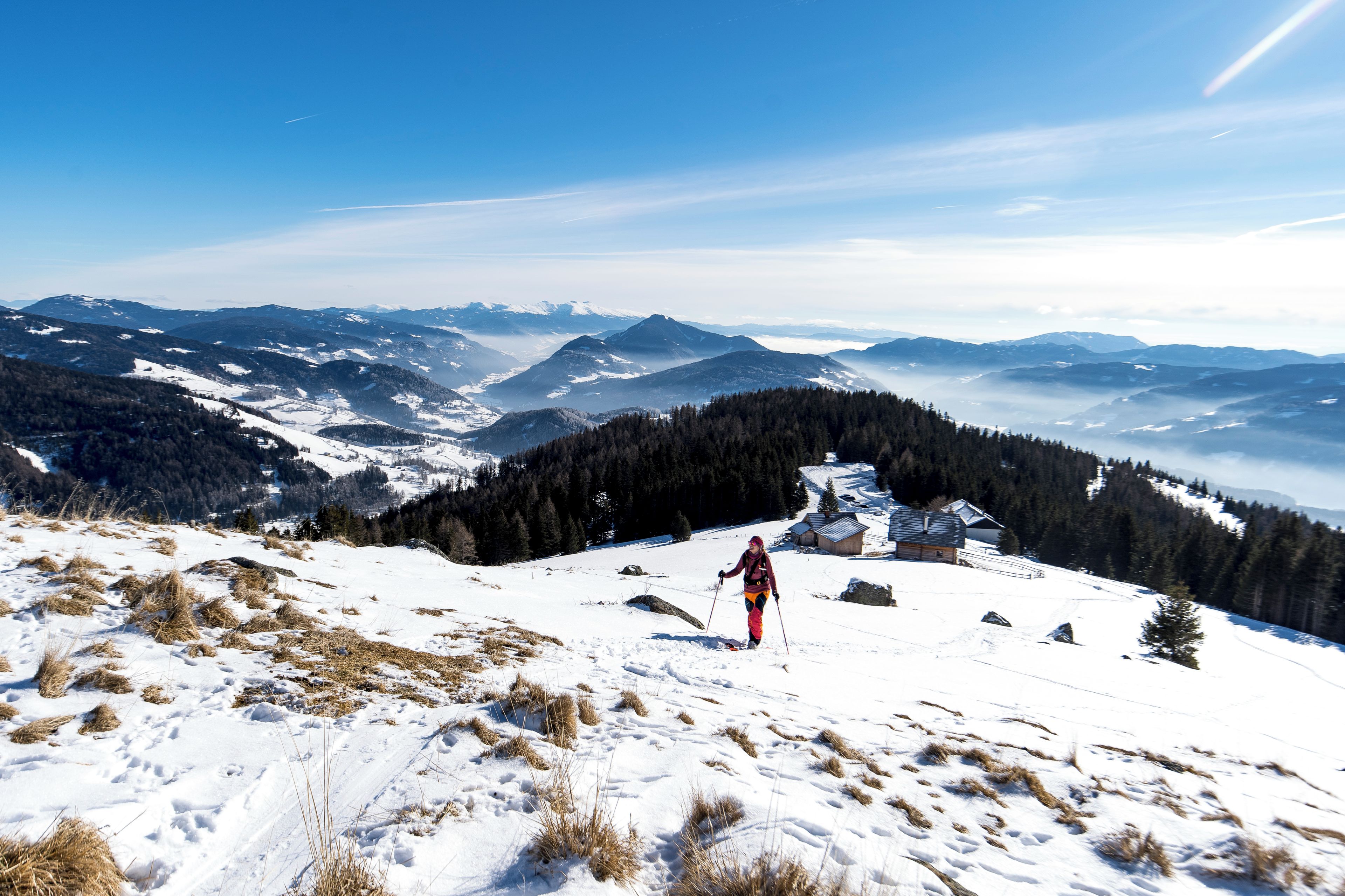 Eine Person beim Skifahren auf einem verschneiten Berg, mit Blick auf entfernte Berge und einen klaren Himmel.