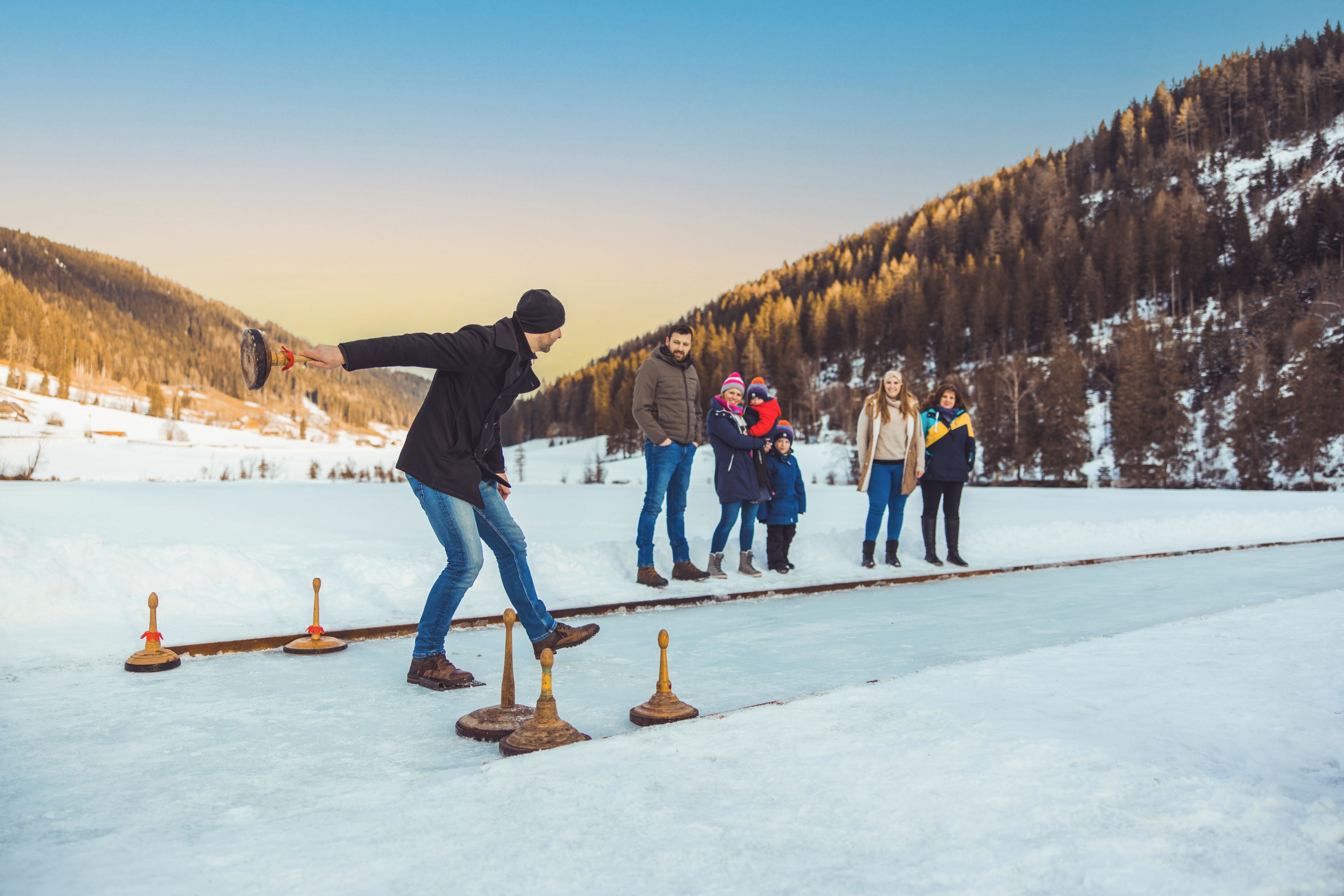 Un gruppo di persone che pratica un'attività invernale su una superficie ghiacciata, con montagne sullo sfondo.