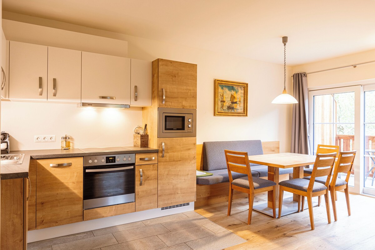 Una cocina moderna con armarios de madera, electrodomésticos de acero inoxidable y un comedor con sillas y mesa de madera.