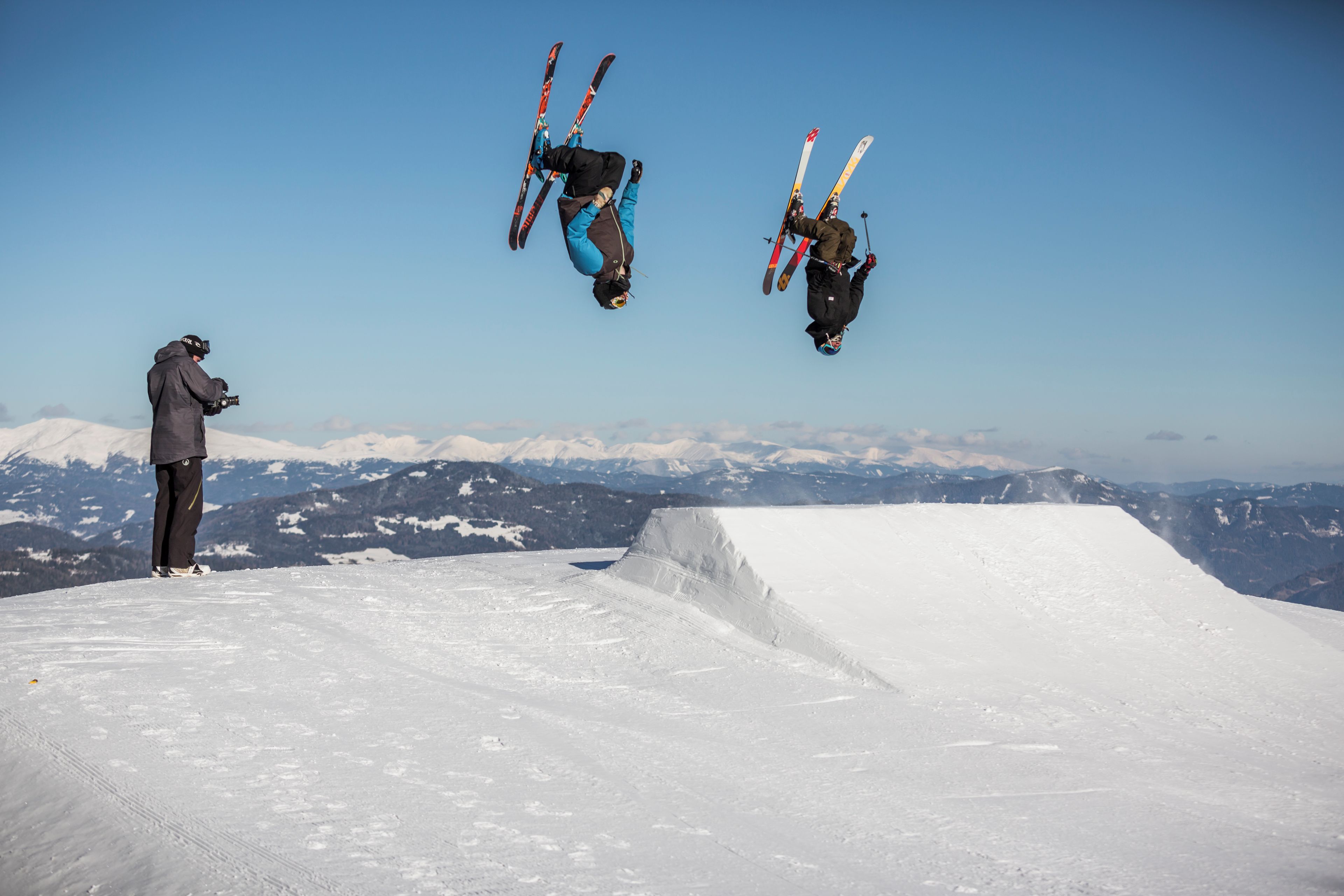 A snowy ski slope with a photographer capturing a skier in mid-air.