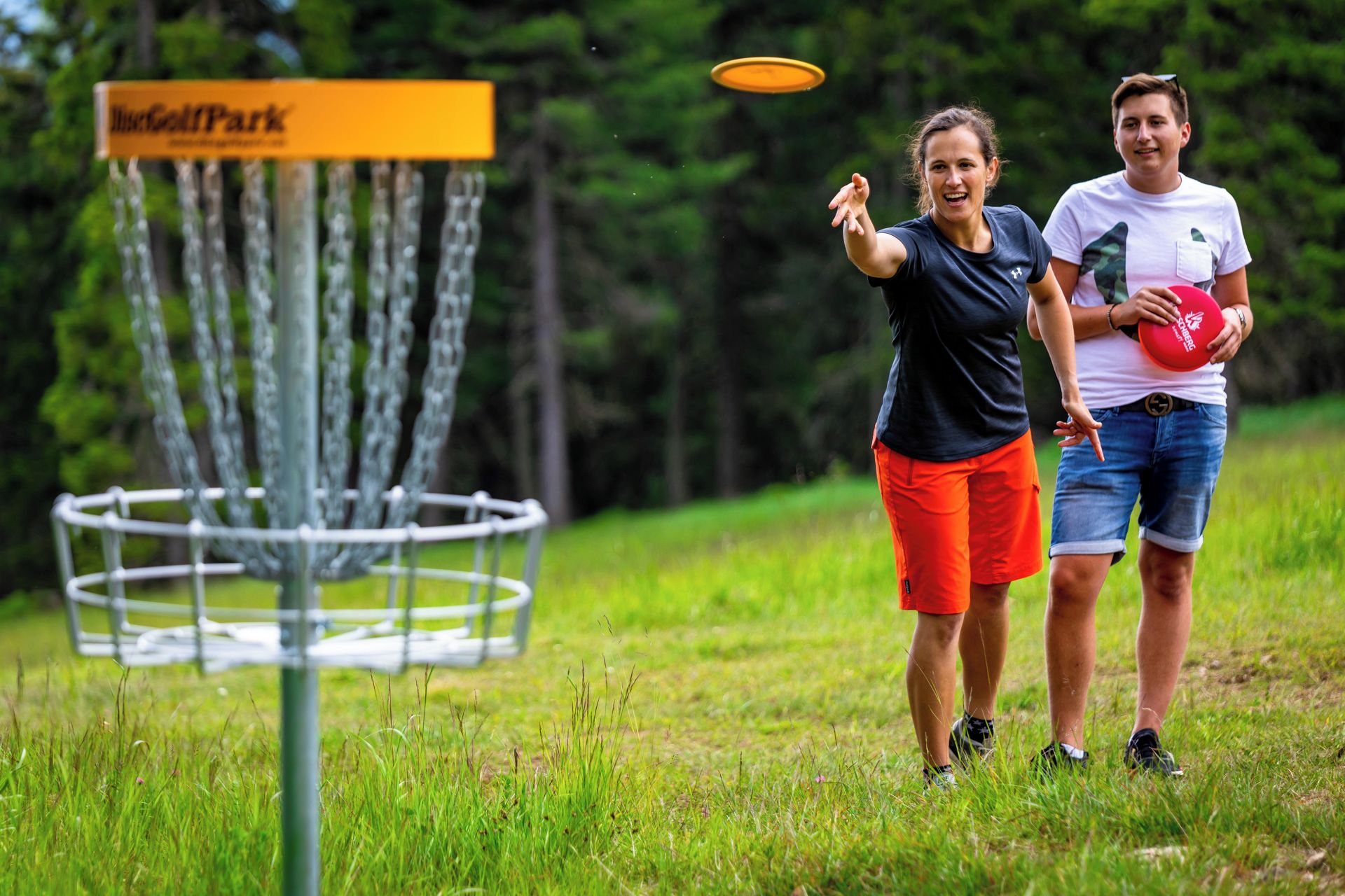Two people playing frisbee near a disc golf course sign.