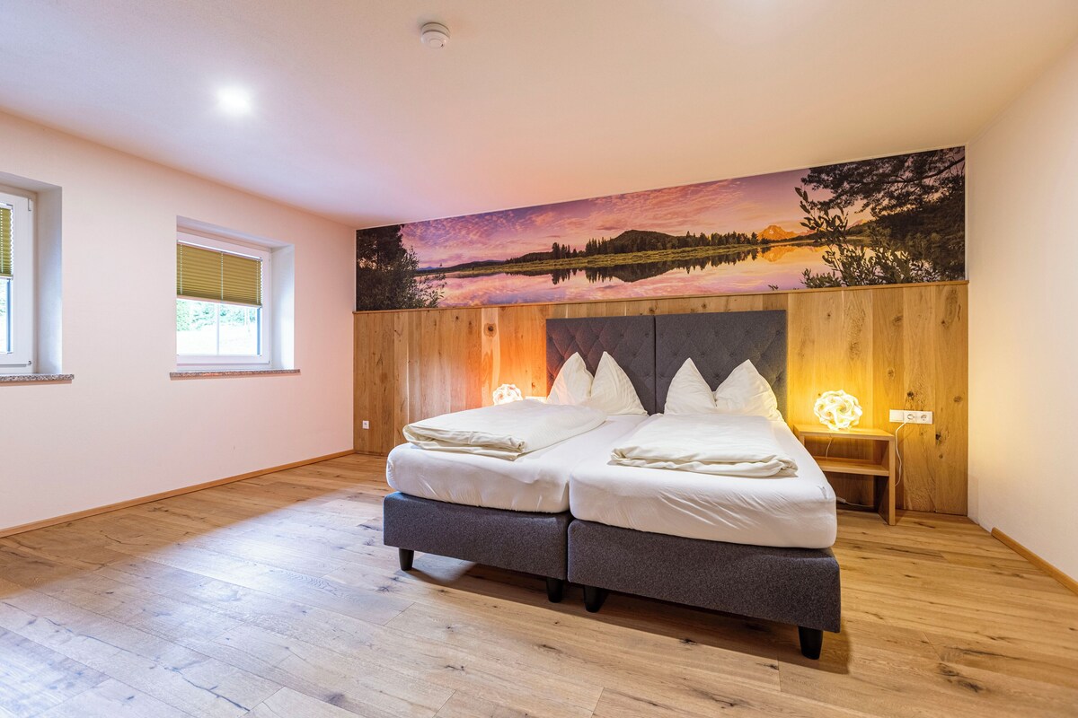 Un dormitorio con cabecera de madera, dos camas, una mesita de noche y una lámpara de pared.