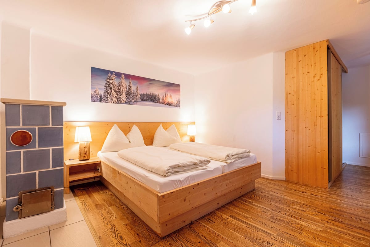 Um quarto com cama de madeira, lareira de pedra e pintura de uma paisagem nevada.