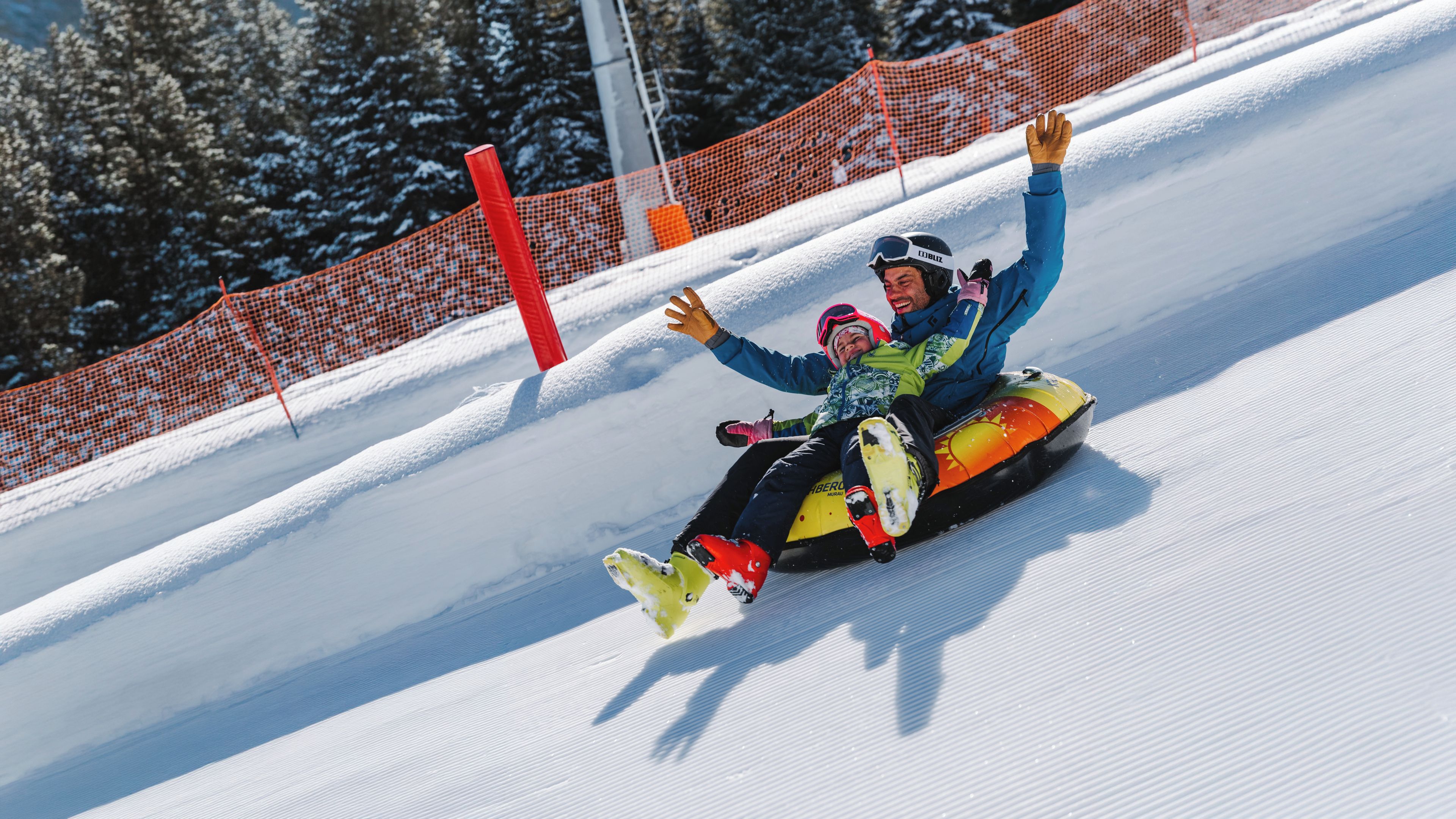 A person on a snow tube on a snowy slope with a safety net in the background.