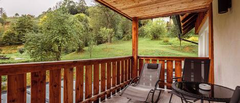 A covered outdoor area with a wooden deck, a table with chairs, and a view of a green landscape.