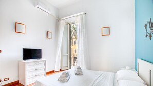 A bedroom with a bed, a TV on a dresser, and a window with curtains.