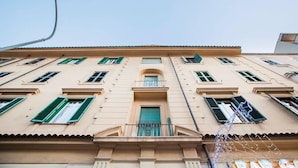 A multi-story building with a central entrance, green shutters, and a balcony.