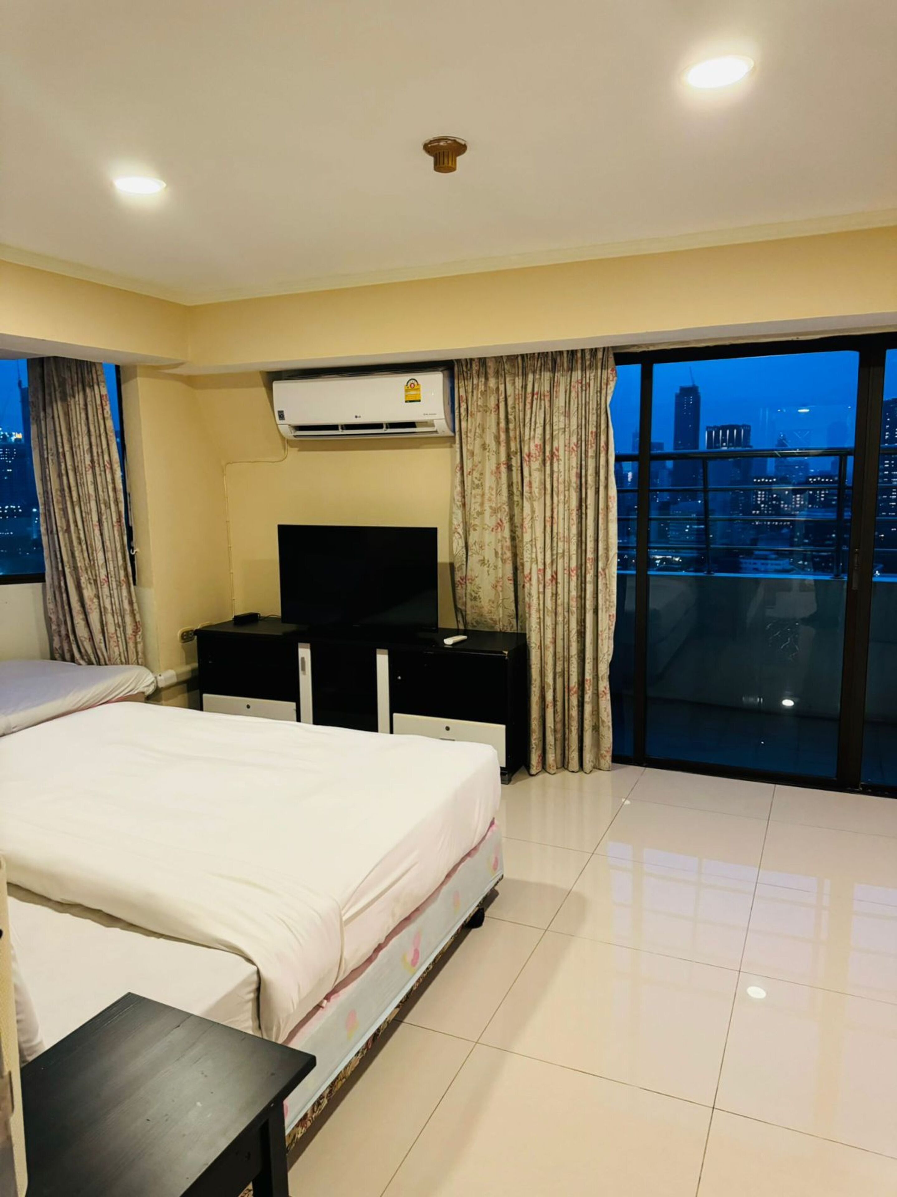 Ein Hotelzimmer mit Bett, Fernseher, Kommode und großem Fenster mit Blick auf die Stadt.