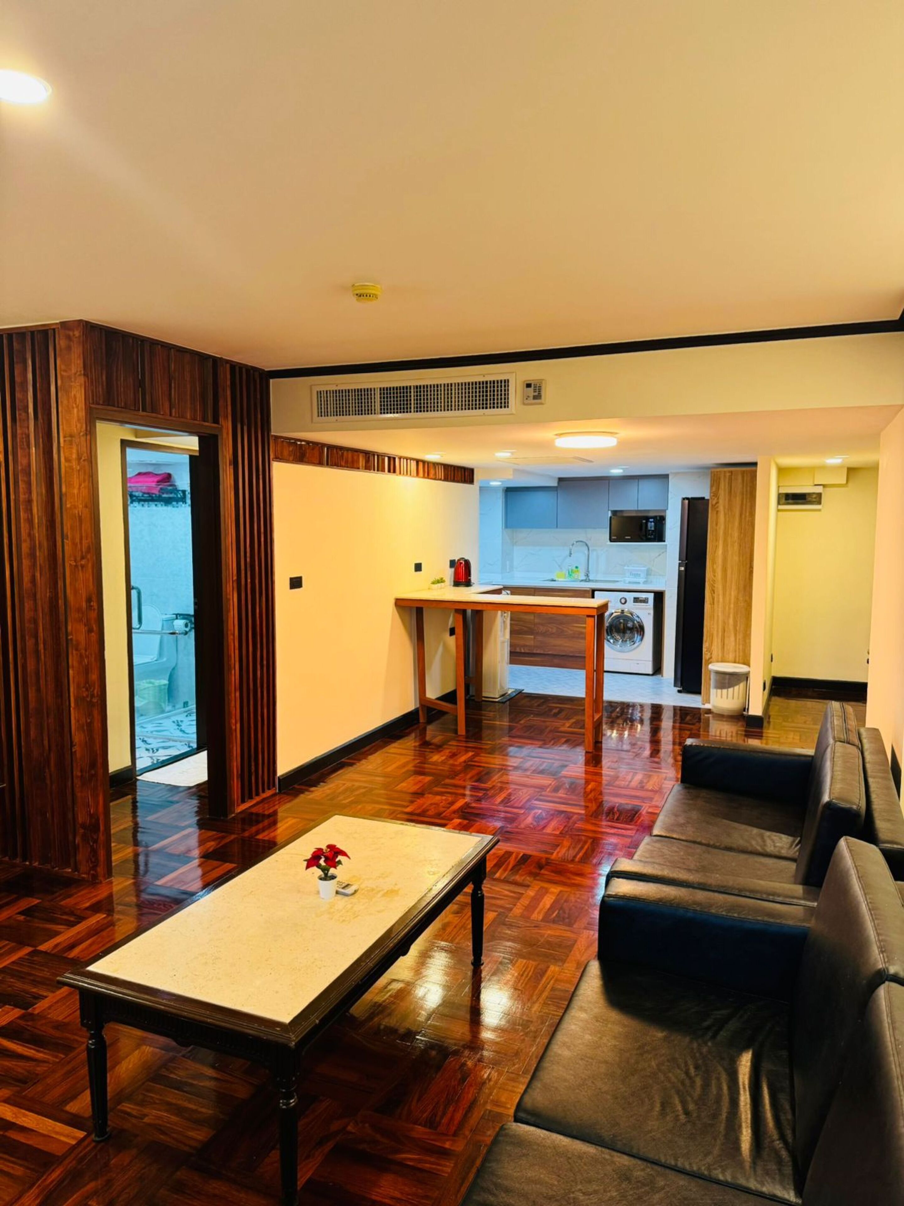 A modern living room with a wooden floor, a coffee table, a sofa, and a kitchen in the background.