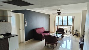 A modern living room with a dark accent wall, a red sofa, a coffee table, and a dining area with a table and chairs. - Direct Rooms at Omni Complex Nana (Bangkok)