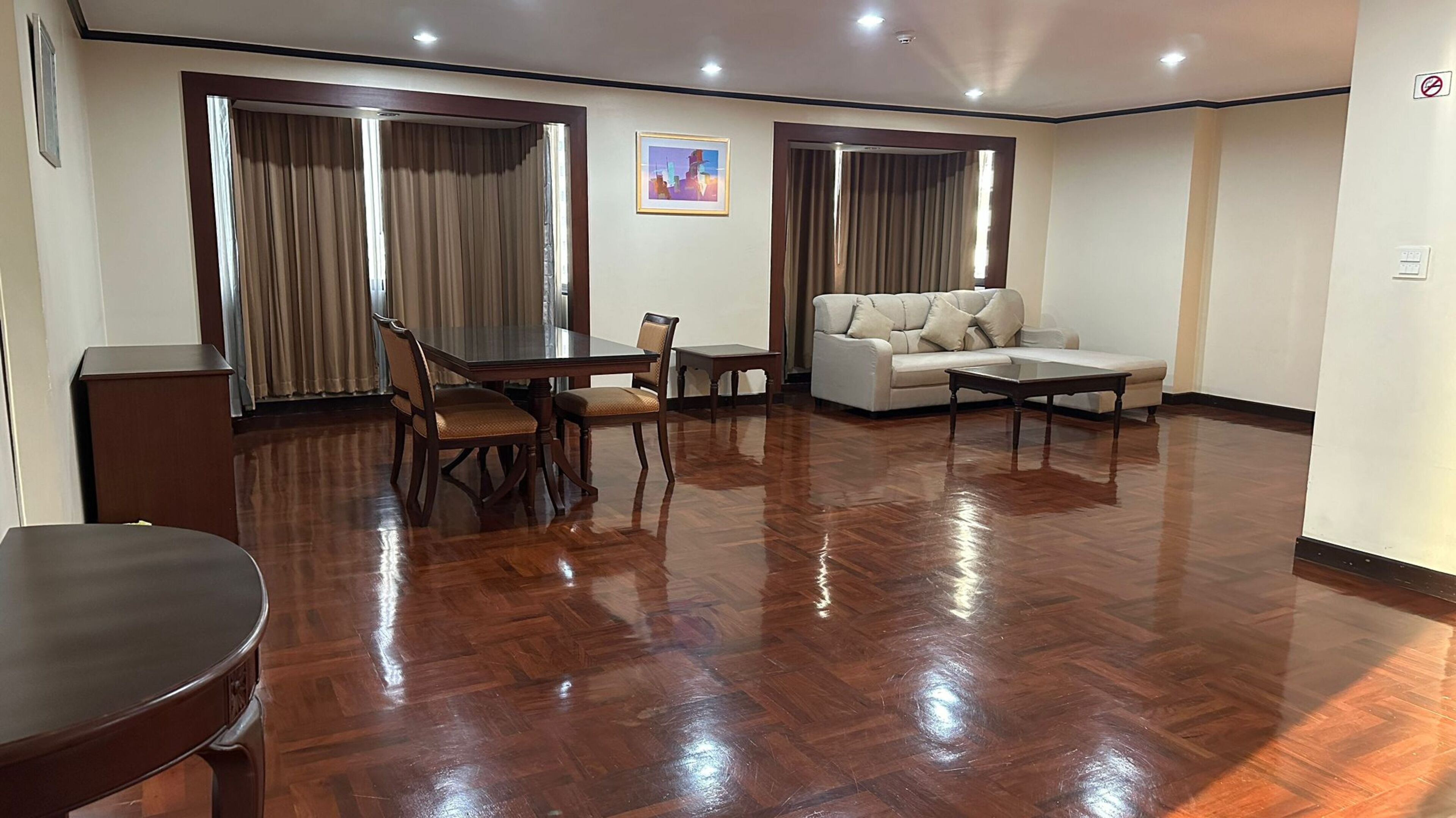 A spacious living room with a wooden floor, a dining table with chairs, a sofa, and a coffee table.