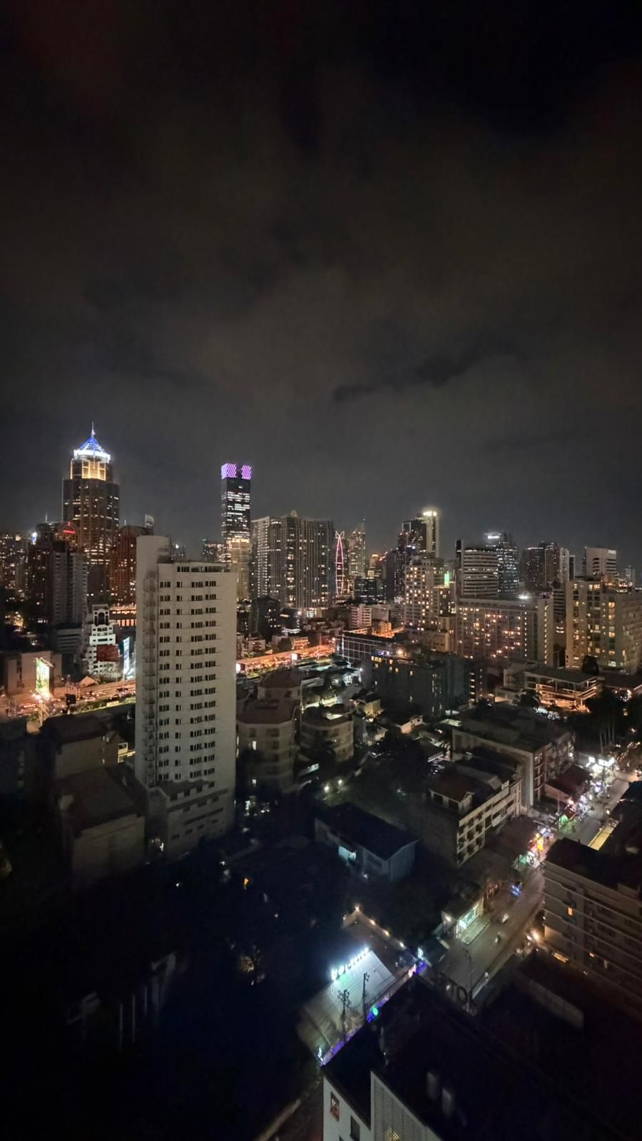 A nighttime cityscape with illuminated buildings and a prominent tower with a spire.