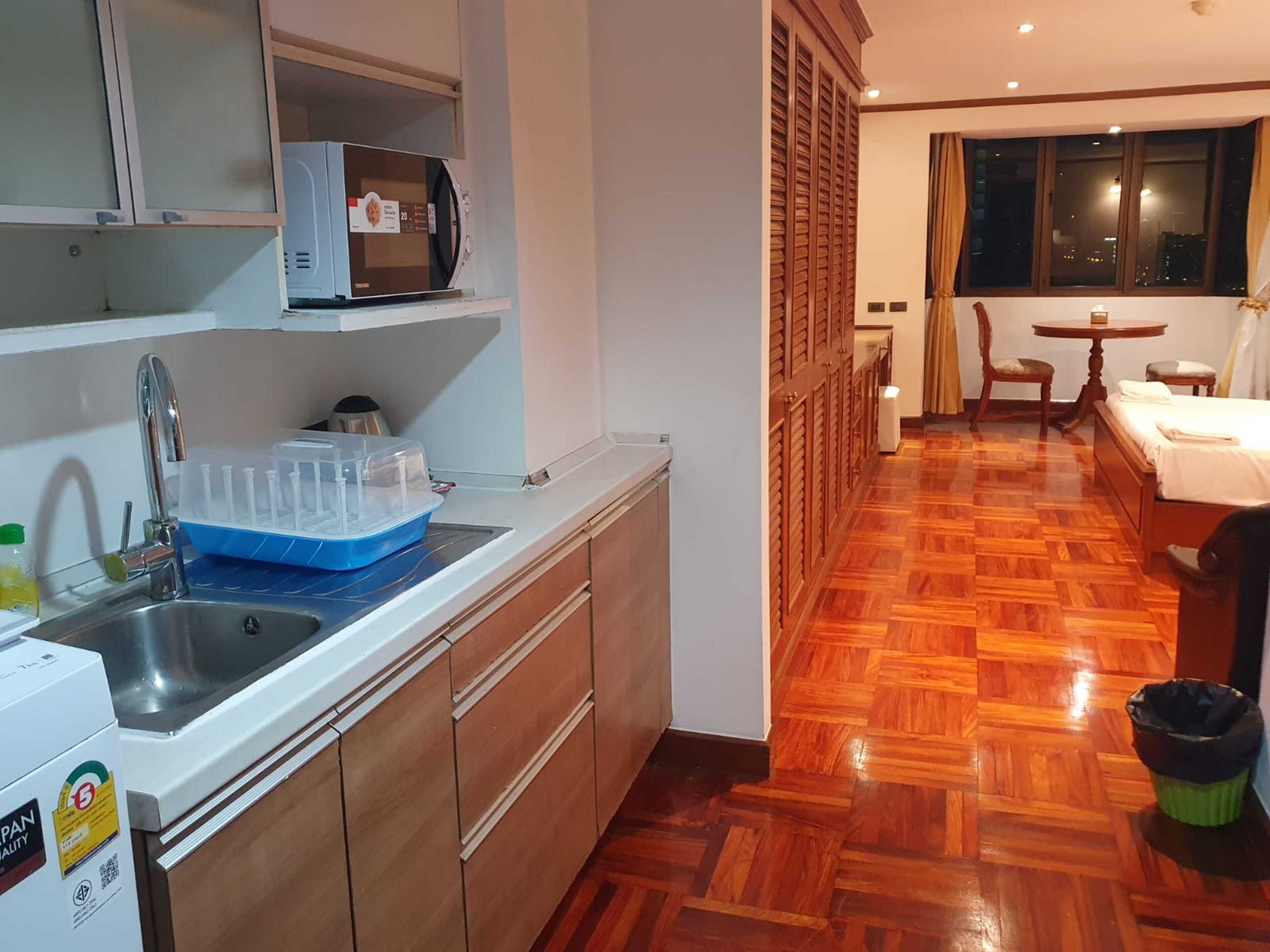 Une cuisine compacte équipée d’un four à micro-ondes, d’un évier et de placards de rangement. On aperçoit à l’arrière-plan un coin repas avec une table et des chaises.