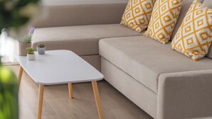 En moderne stue med en beige modulsofa, et hvidt sofabord og mønstrede puder. To billeder hænger over sofaen.