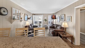 A spacious living area with a dining table, two couches, and a kitchen area with a refrigerator and stove. - A Place at the Beach III 9520-2B Summer Escape at Myrtle Beach Ocean View Condo (Myrtle Beach)