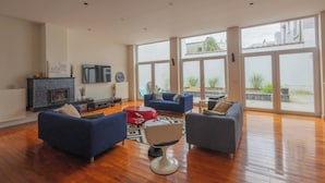 A spacious living room with a fireplace, multiple sofas, and large windows offering views of the outdoors. - Chambres Cosy dans Une Grande maison (Brussels)