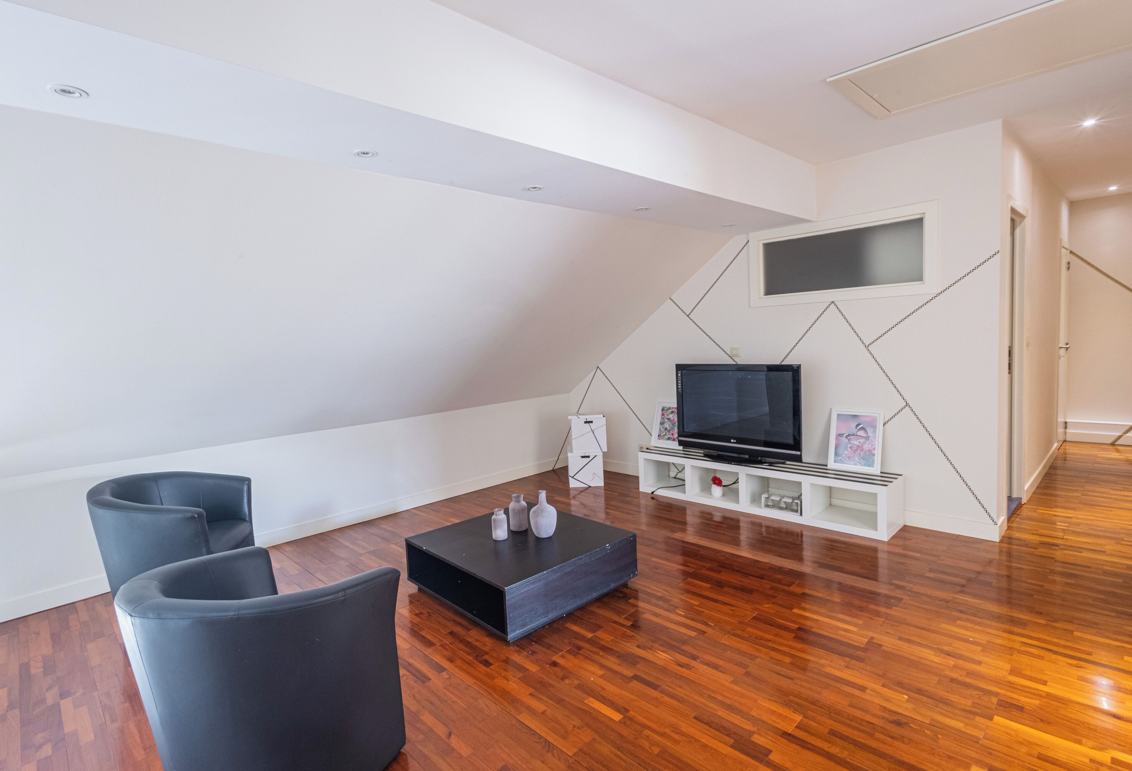 A modern living room with a black coffee table, two black chairs, a flat-screen TV, and a white entertainment unit.