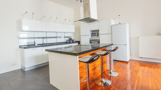 A modern kitchen with a central island, bar stools, white cabinetry, a microwave, oven, and a refrigerator. - Chambres Cosy dans Une Grande maison (Brussels)