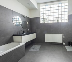 A modern bathroom with a bathtub, a sink with a mirror, a window with a view, and a radiator.