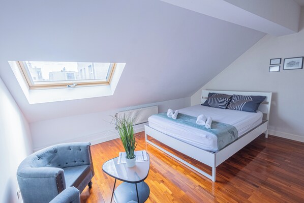 A bedroom with a bed, a chair, a small table, and a skylight. - Chambres Cosy dans Une Grande maison (Brussels)