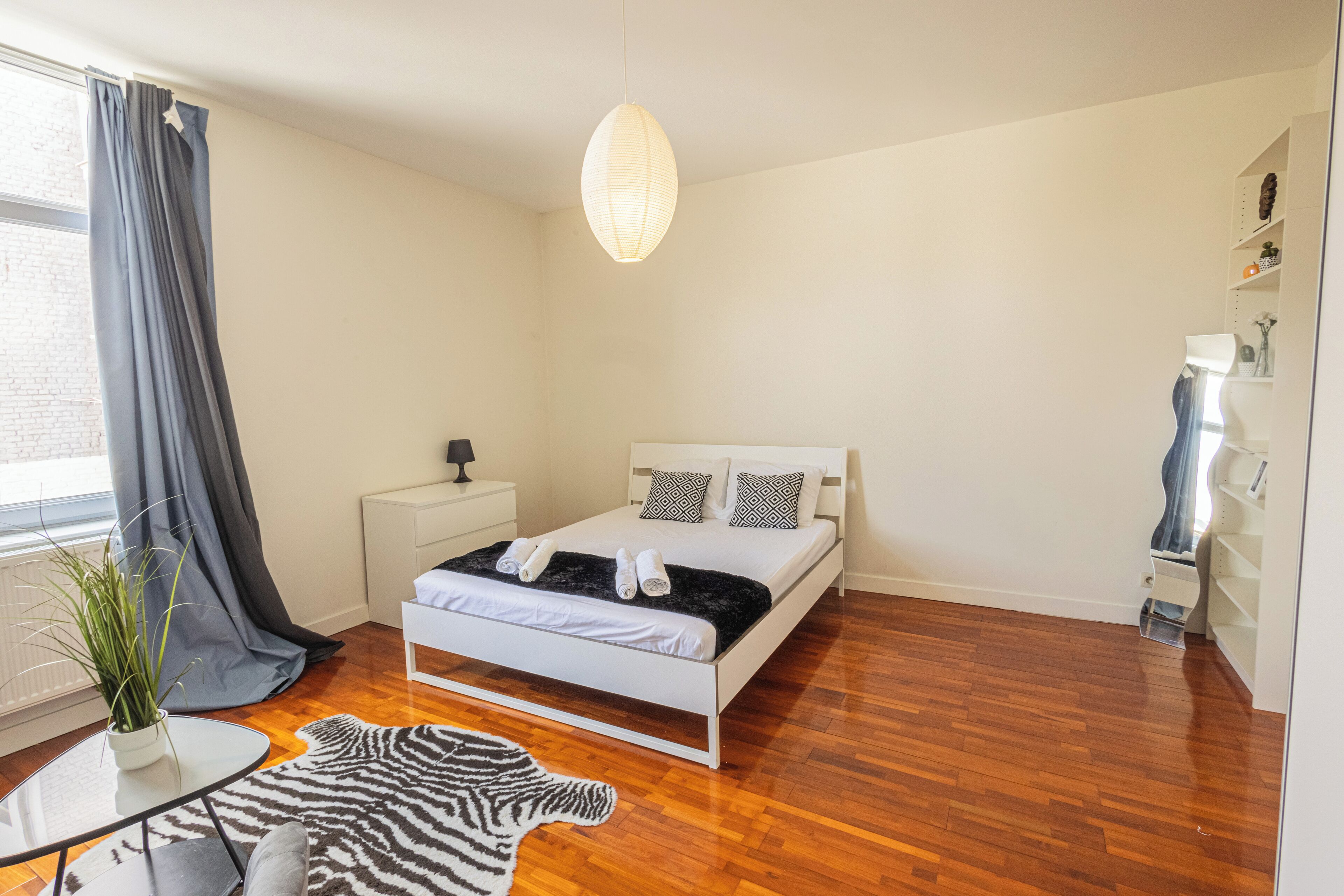 A bedroom with a bed, bedside table, lamp, and a hanging light fixture.