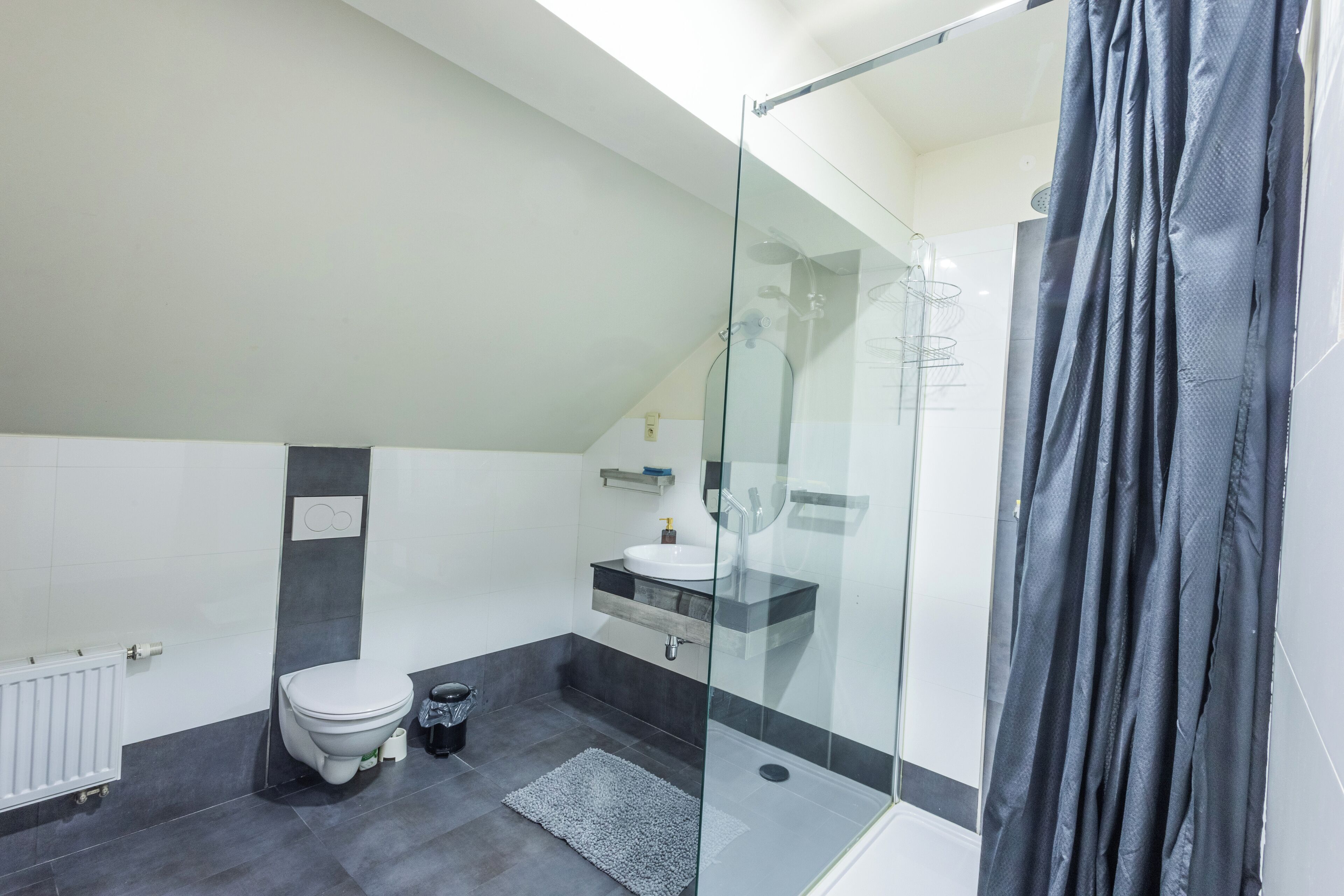 Une salle de bain moderne avec une douche à parois de verre, des toilettes blanches et un sol carrelé foncé.