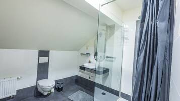 Une salle de bain moderne avec une douche à parois de verre, des toilettes blanches et un sol carrelé foncé.