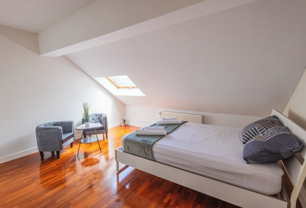 A loft-style bedroom with a sloped ceiling, a skylight, a bed with pillows, a chair, and a small table. - Chambres Cosy dans Une Grande maison (Brussels)
