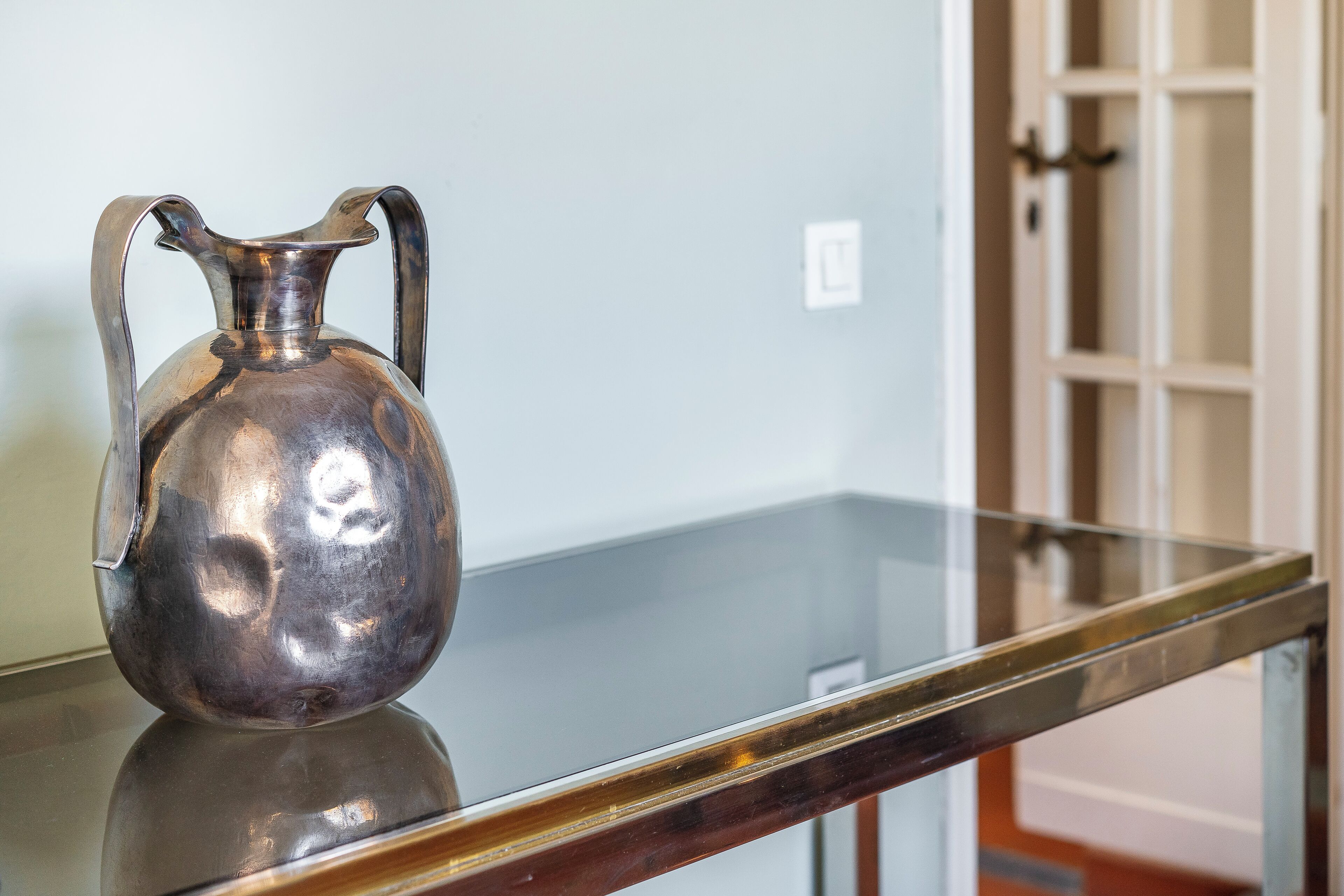A metallic pitcher on a reflective glass table.