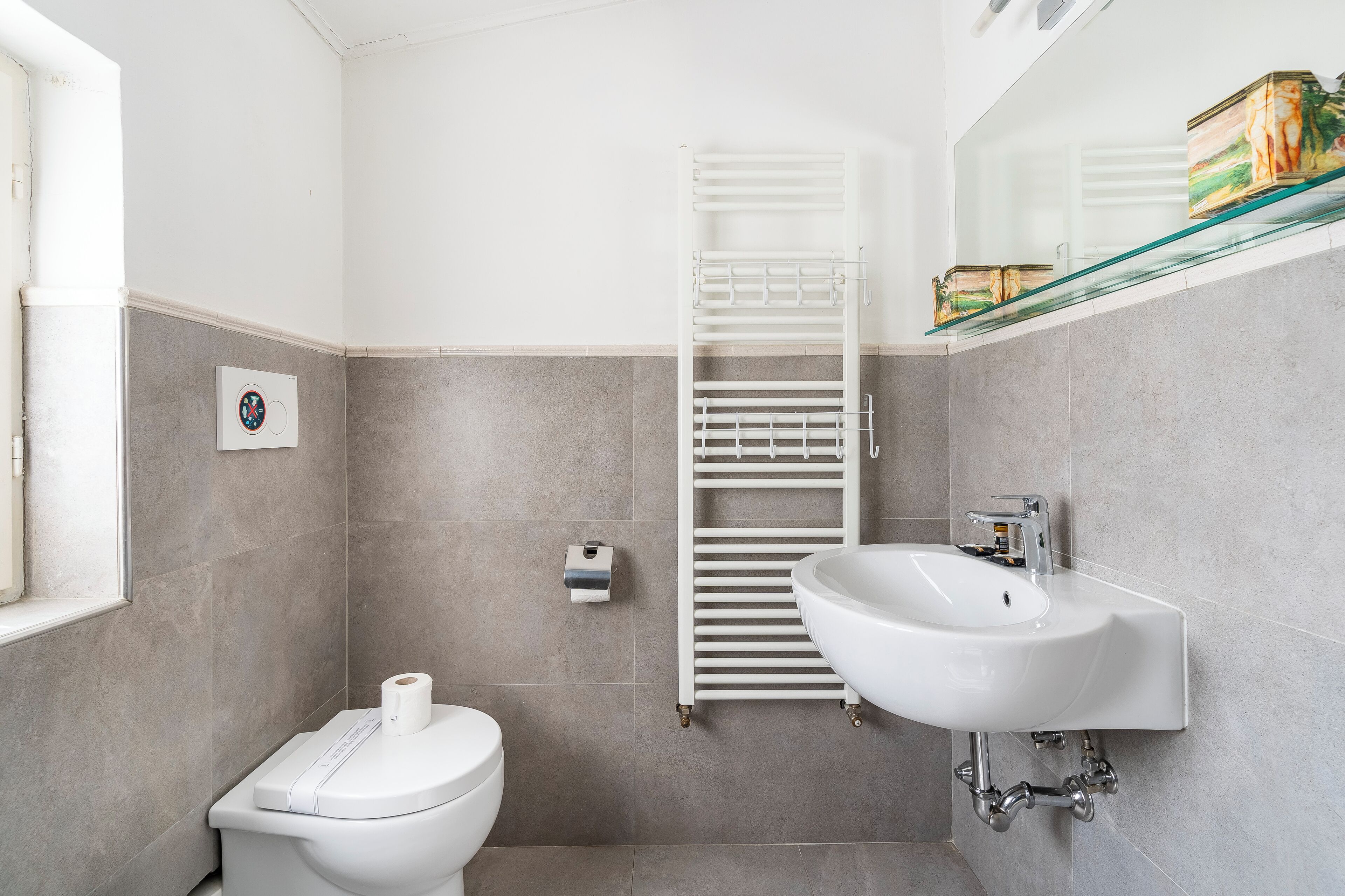 A modern bathroom with a toilet, a glass shelf with decorative items, a white sink, and a towel rack.