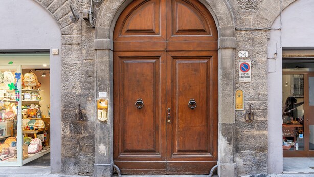 A large wooden double door with a stone archway, a 'No Parking' sign, and a small shop with colorful items visible through the window. - Maggio 54 - Three Bedroom Apartment, Sleeps 6 (Florence)