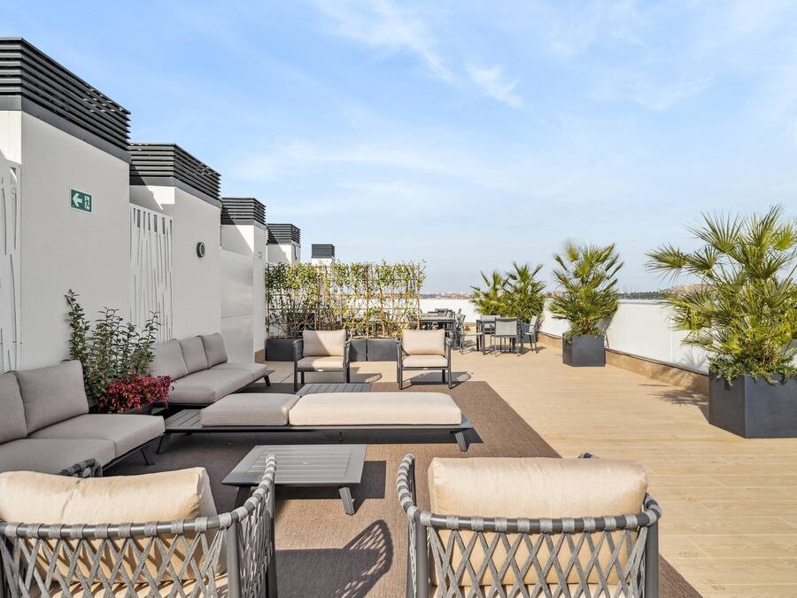 A rooftop terrace with outdoor seating, including sofas and chairs, and potted plants.