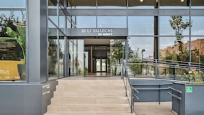 A modern building entrance with a glass facade, a sign reading "BEXT VALLECAS BY HABYT", and a staircase leading to the entrance. - Truliving Vallecas by Habyt (Madrid)