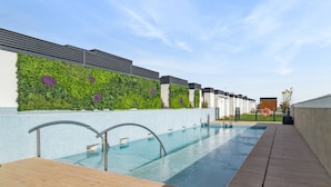A modern outdoor swimming pool with a tiled deck, a green vertical garden wall, and a clear blue sky. - Truliving Vallecas by Habyt (Madrid)